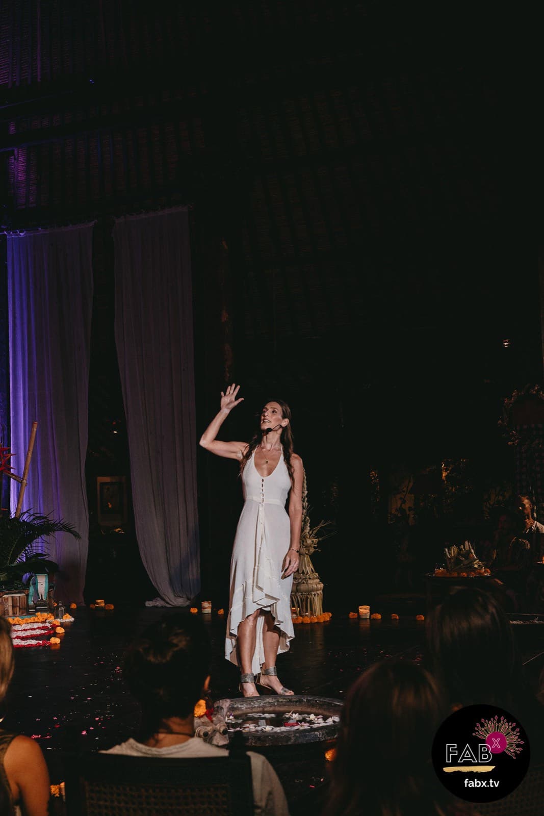 Arja Hendrikx in a white dress with one arm raised on a dark theatrical stage