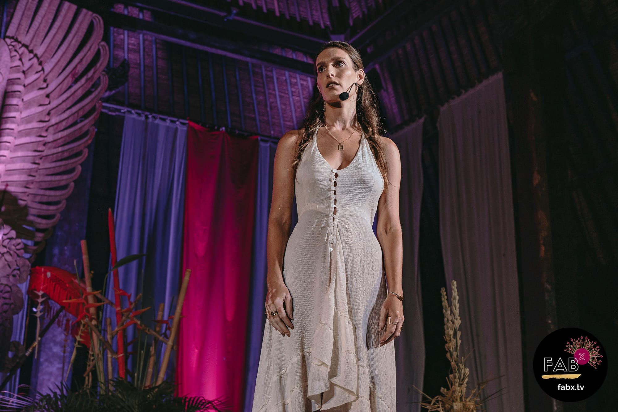 Arja Hendrikx in a white dress standing on a decorated stage hung with deep coloured fabric