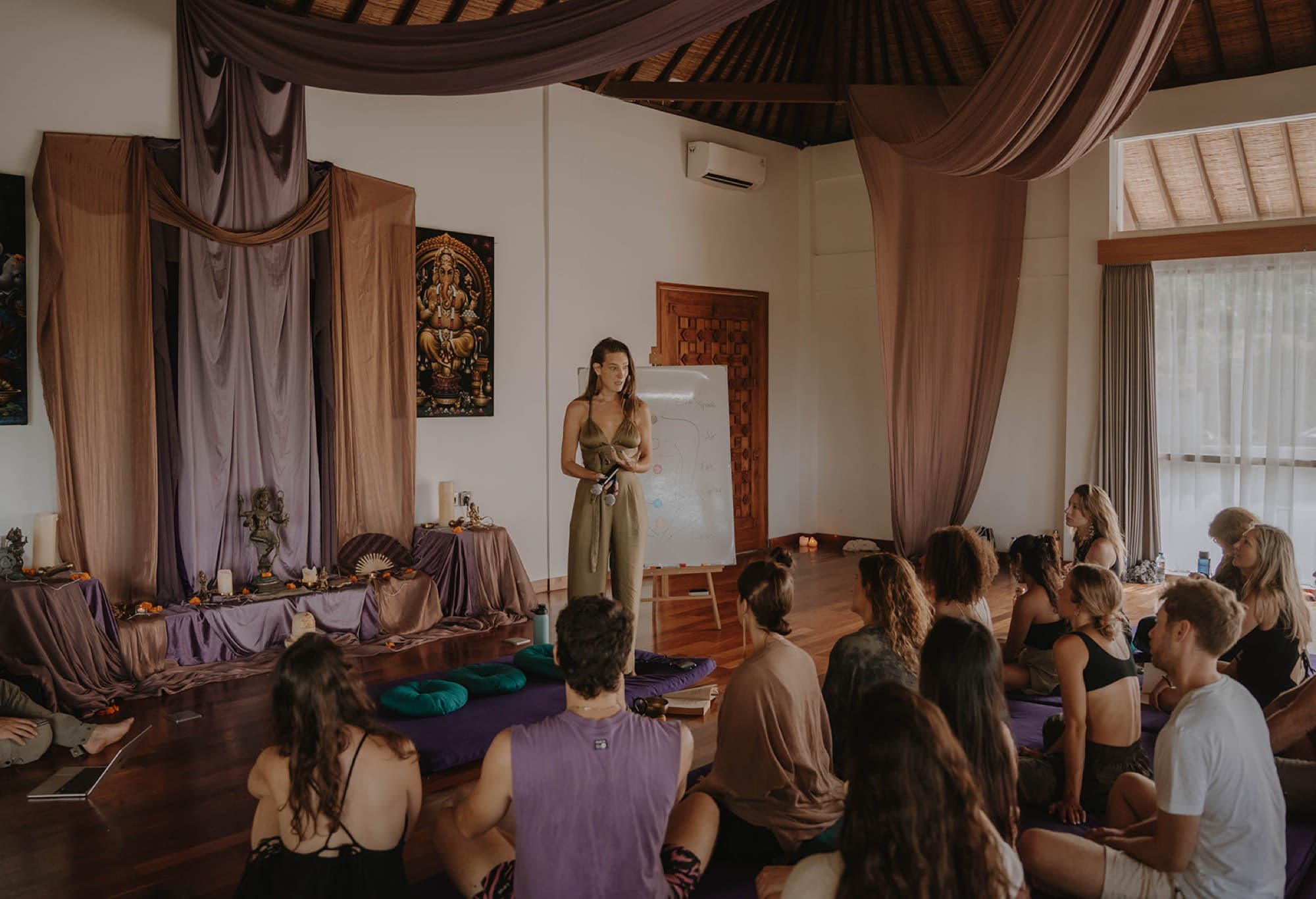 Arja Hendrikx teaching a seated group in a temple room, a diagram drawn on the whiteboard behind her
