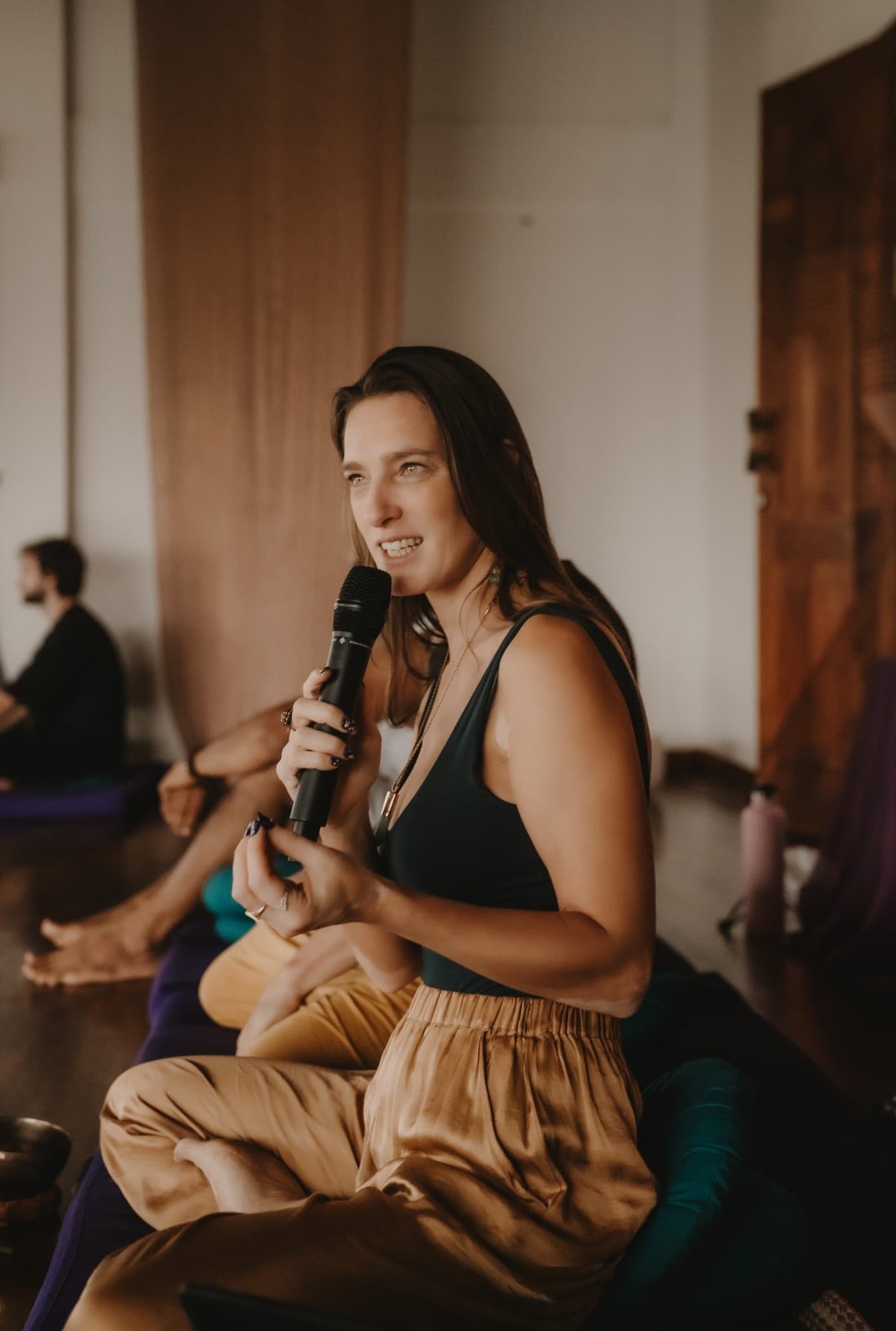 Arja Hendrikx sitting cross legged with a microphone, smiling as she answers a question from the group